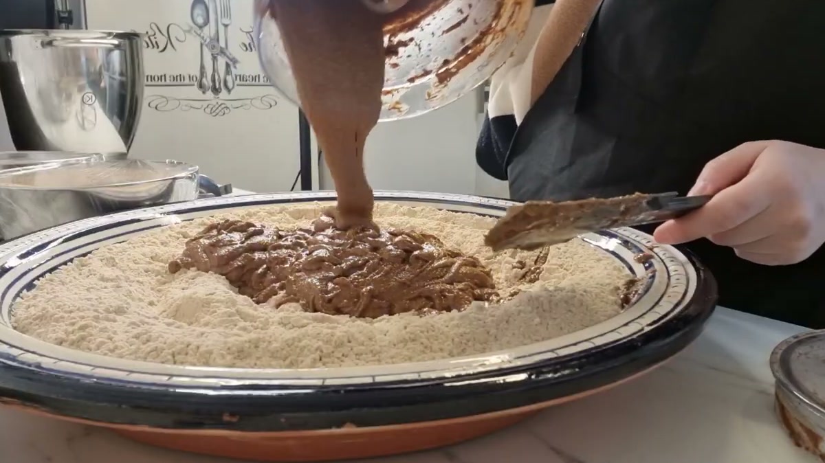 Pouring the ground almond paste over the toasted flour in a large dish