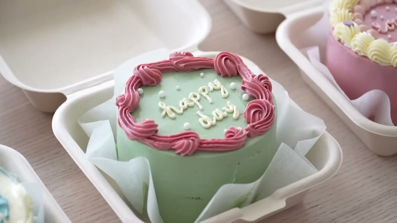 Sage green bento cake packed in a paper burger box with a pink cake behind it