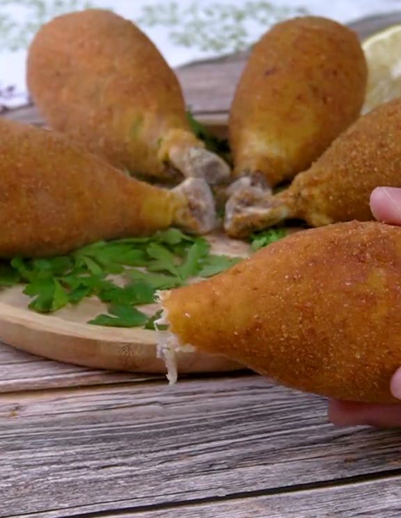 Golden chicken drumstick croquettes with the bones sticking out, on a wooden board with parsley