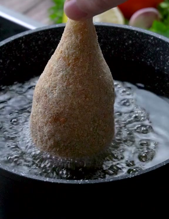 Lowering a breaded drumstick croquette into hot oil