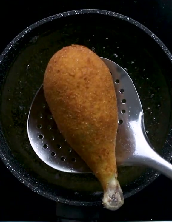 A golden fried chicken drumstick croquette on a slotted spoon