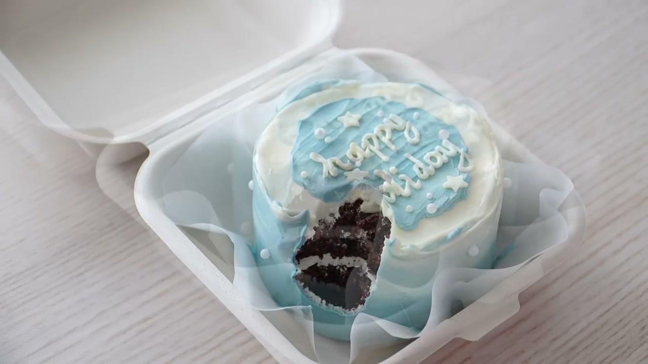 A blue bento cake in its box with a slice cut out, showing the chocolate layers inside