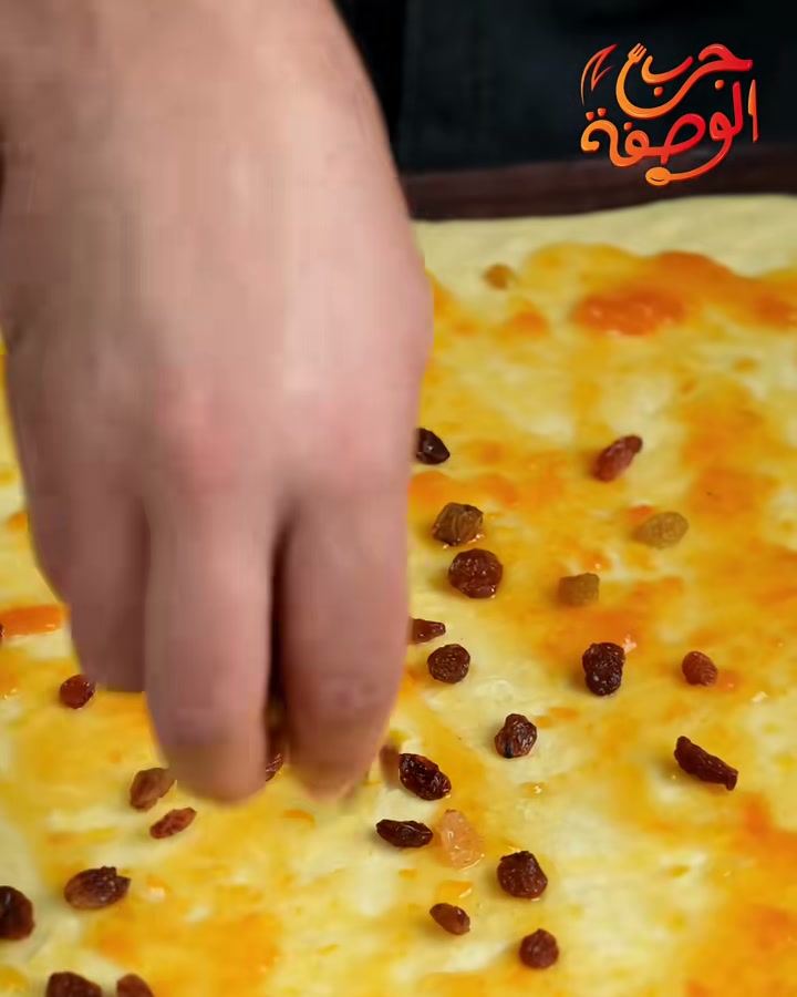 Scattering raisins over apricot jam spread on the dough