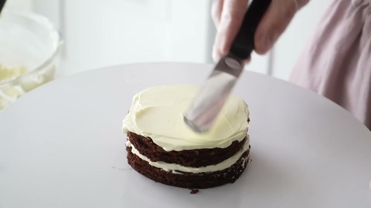 Spreading vanilla buttercream between chocolate cake layers for this bento cake recipe