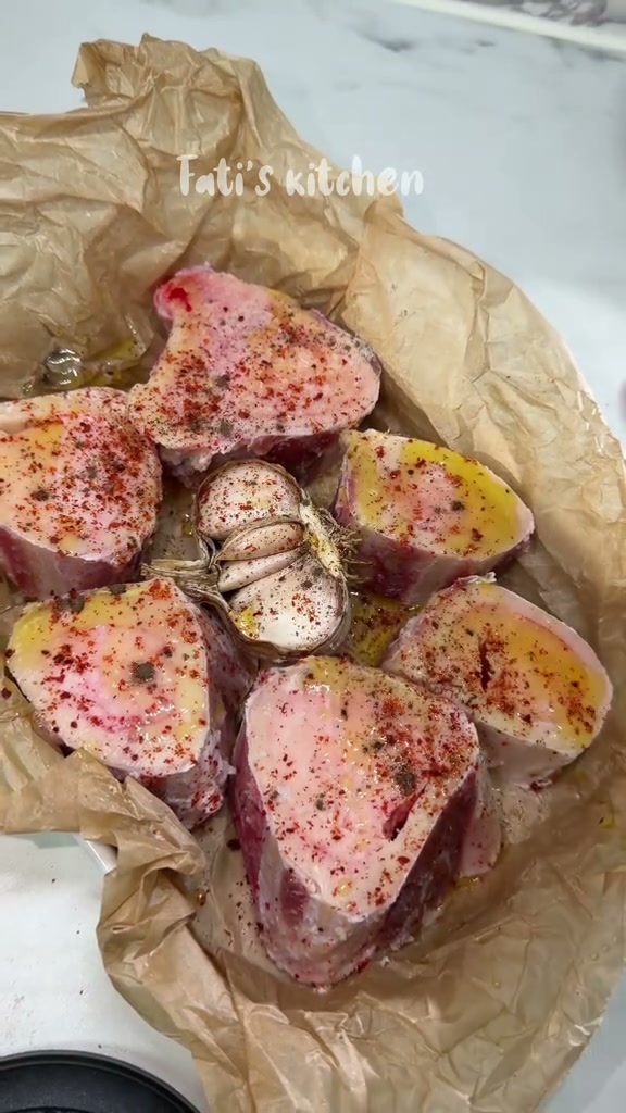Raw beef marrow bones on parchment with a halved garlic head, olive oil and red pepper