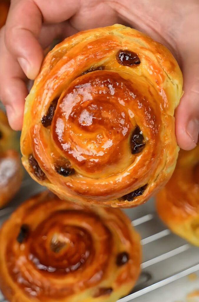 Moroccan chnek: a glossy laminated brioche swirl with raisins held in two hands