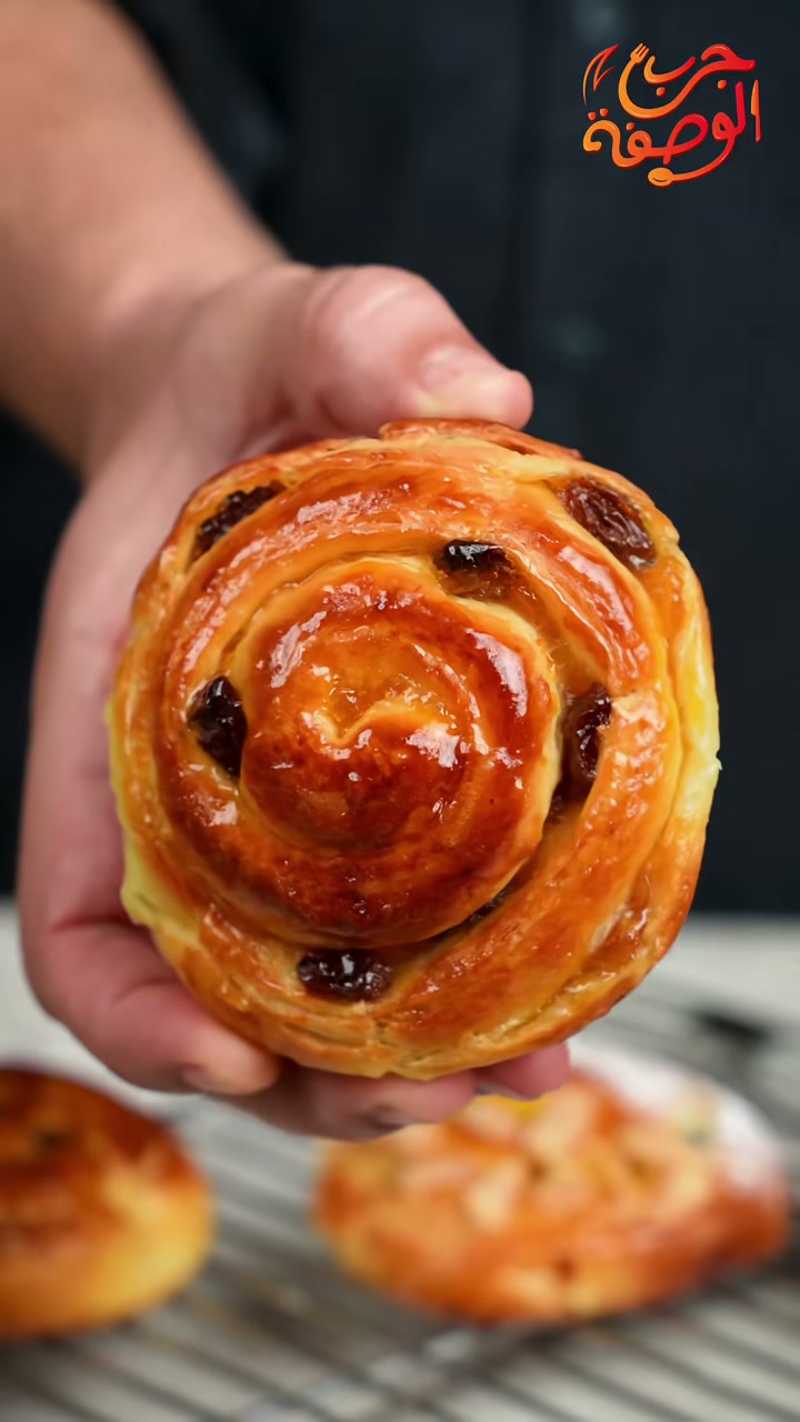Moroccan chnek: a glossy laminated brioche swirl with raisins held in two hands