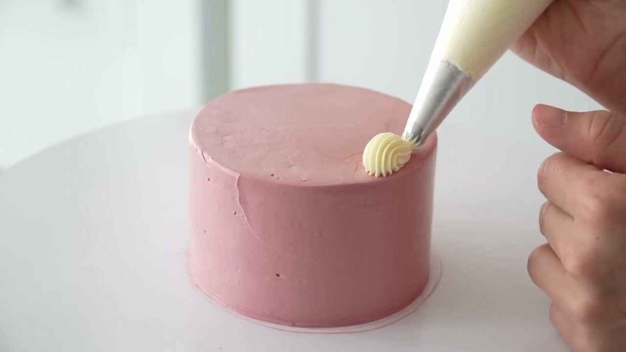 Piping a buttercream shell border on top of a pink bento cake
