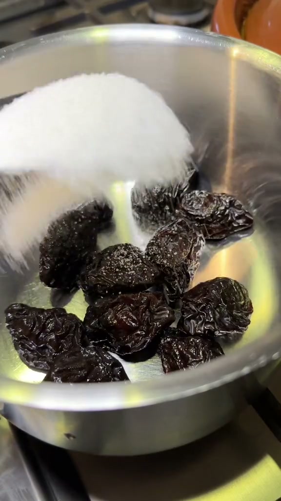Prunes with sugar and a cinnamon stick in a saucepan