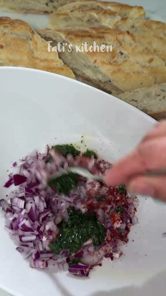 Chopped red onion with green herbs, cayenne pepper and salt in a white bowl