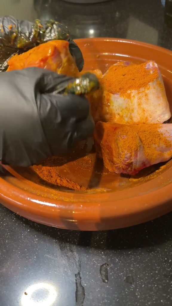 Rubbing olive oil and spices into lamb shanks with gloved hands