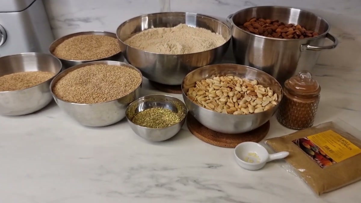 Sellou ingredients in bowls: toasted flour, almonds with skin, sesame seeds, peanuts, fennel seeds and spices