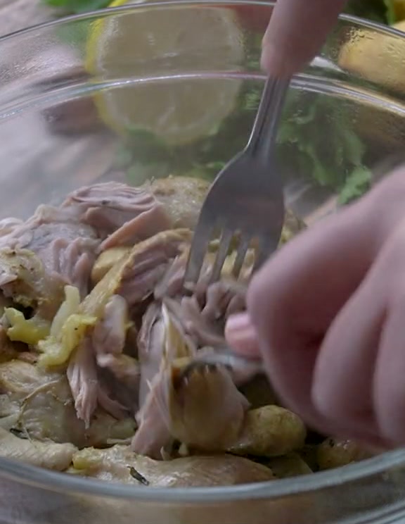 Shredding the cooked chicken off the bone with a fork